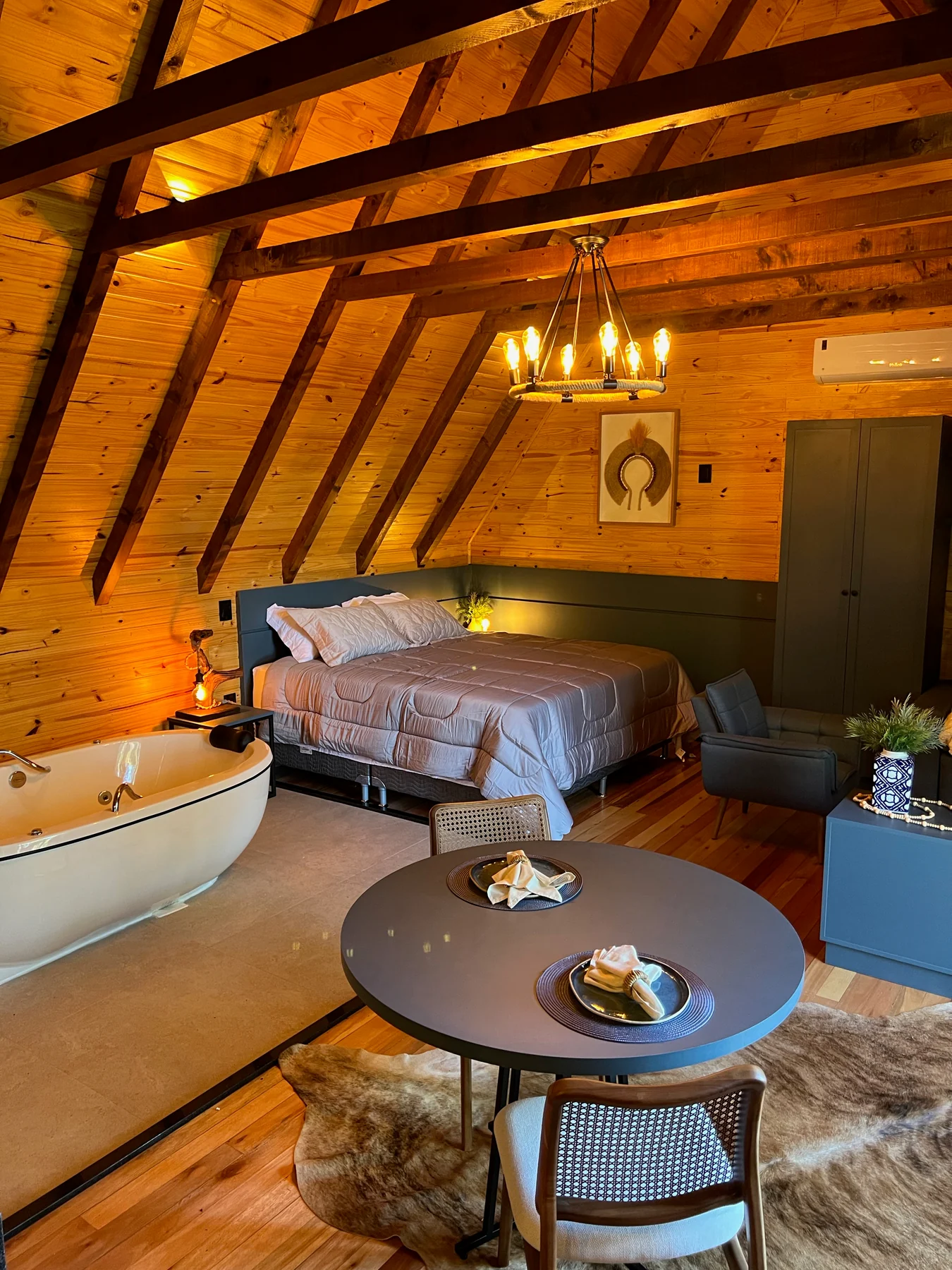 Interior de uma cabana do Taboo Refúgio, com cama arrumada, banheira e estrutura de madeira